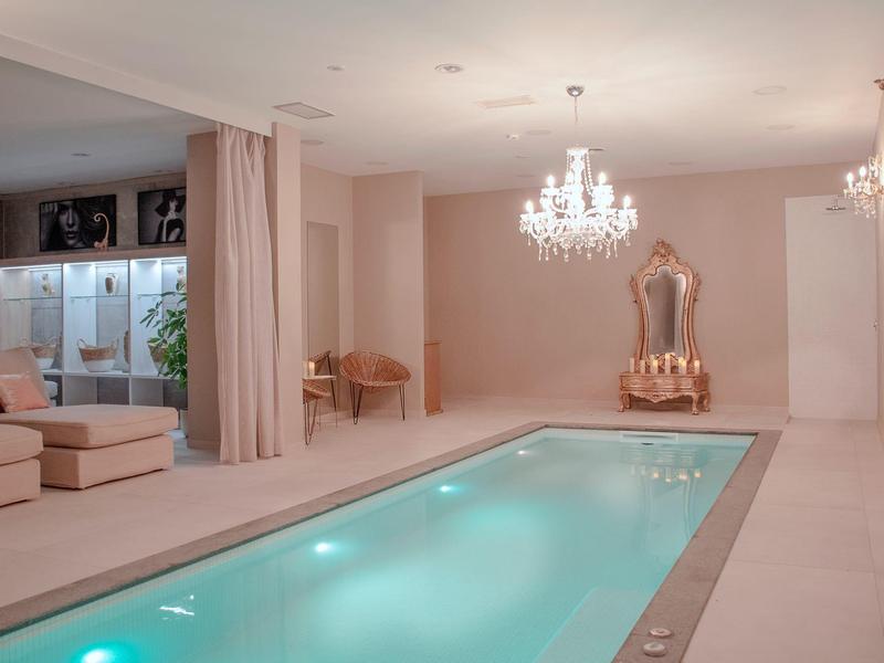 Área elegante de piscina interior con cómodos asientos y candelabro bajo luz cálida.