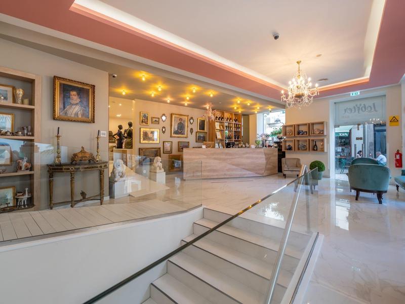 Lobby de hotel luminosa con mármol blanco, escaleras, recepción y iluminación elegante.