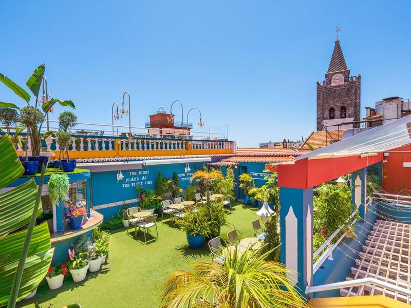Terraza con césped artificial, plantas y estructura de hierro con toldo en un entorno urbano soleado