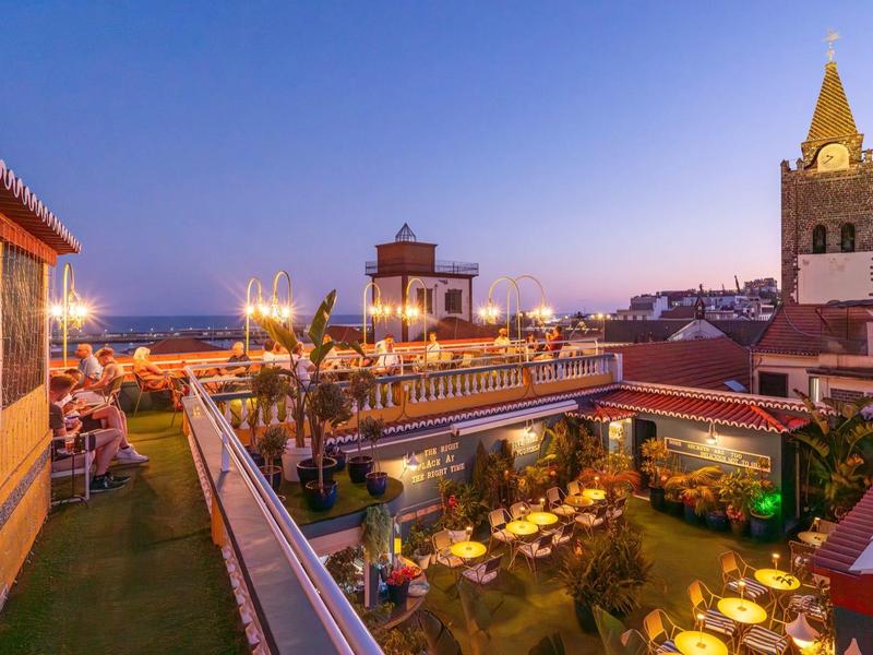 Terraza en la azotea de un hotel con asientos y luces al atardecer.