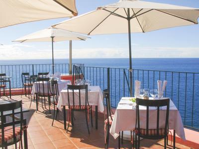 Terrasse mit Tischen und Stühlen, Sonnen- und Meeresblick, helle Sonnenschirme schützen vor Sonne.