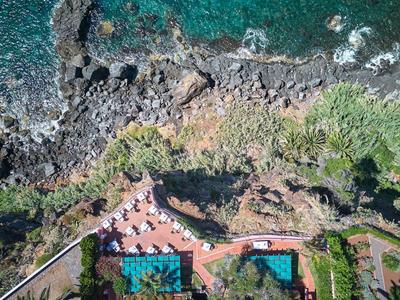 Dachansicht von zwei roten Häusern mit Pools, umgeben von Garten, Felsen und türkisfarbenem Meer.