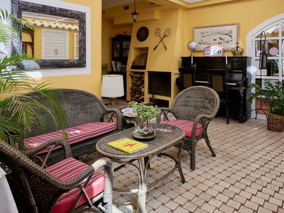 Gemütliche Terrasse mit Rattanmöbeln, gepolsterten Kissen, Pflanzen und gelber Wandgestaltung.