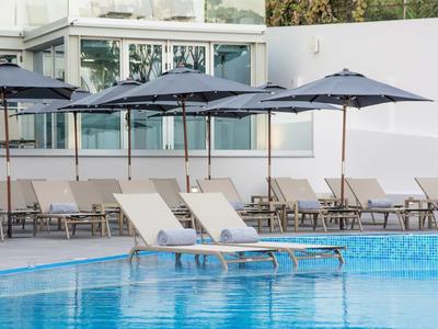 Moderner Poolbereich mit weißen Liegestühlen und blauen Sonnenschirmen vor hellem Haus.