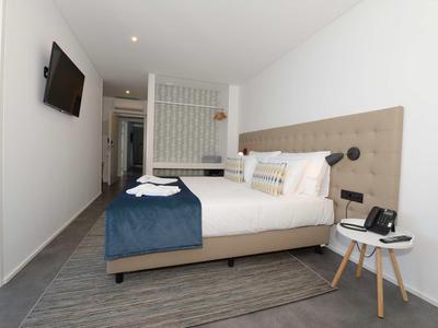 Moderne hotelkamer met tweepersoonsbed, muur-tv en nachtkastje, ingericht in neutrale tinten.