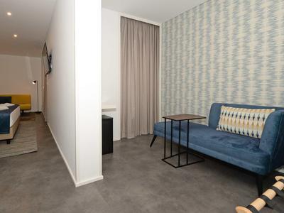 Hotelkamer met blauwe bank, patroonmuur, kleine tafel en bedgedeelte gescheiden door een halve muur.