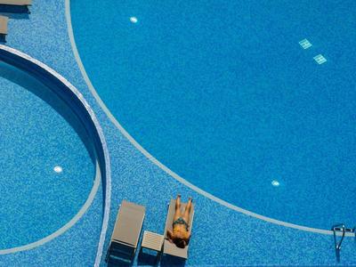 Leeg zwembad met blauw water en twee ligstoelen ernaast in zonnig weer.