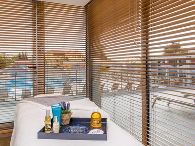 Hotelbalkon met houten jaloezieën, witte ligstoel en dienblad met toiletartikelen en kaarsen.