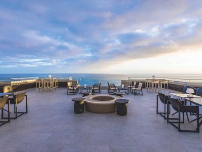 Ruim buitenterras met zitplaatsen en uitzicht op de oceaan onder een gedeeltelijk bewolkte lucht.