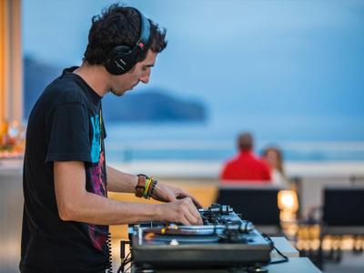 Junger DJ mit Kopfhörern legt an einem DJ-Pult am Strand auf.