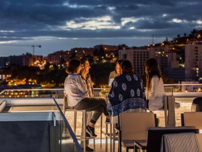 Drie mensen die genieten van drankjes op een dakterras met uitzicht op de stad bij schemerlicht.