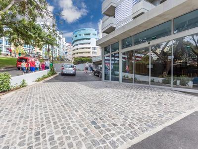 Moderne hotel ingang met kasseien oprijlaan, glazen gevel en geparkeerde voertuigen buiten.