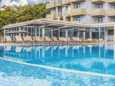 Buitenzwembad met ligbedden en een gebouw omringd door bomen bij een hotel.