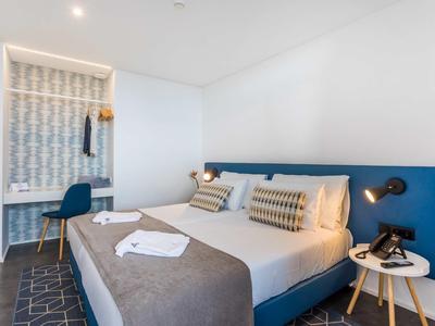 Moderne hotelkamer met groot bed, nachtkastje, bureau en minimalistische inrichting in neutrale tinten.