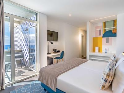 Modernes Hotelzimmer mit Doppelbett, Schreibtisch, Balkon und farbenfrohen Wanddekorationen