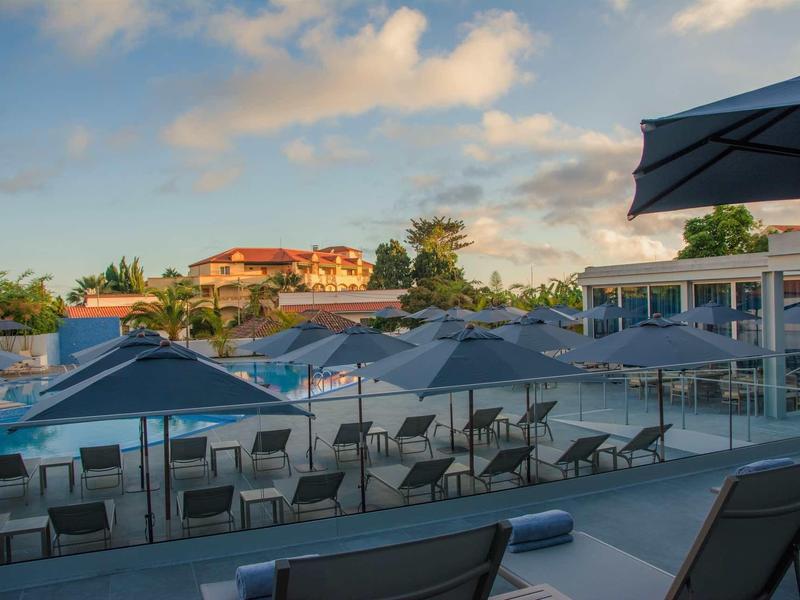Buitenterras met tafels, stoelen en parasols onder een deels bewolkte lucht.