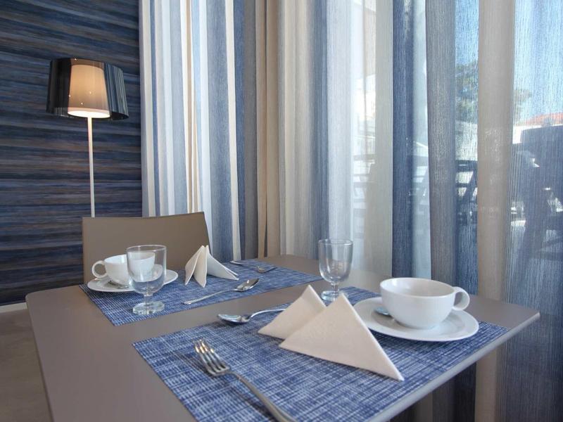 Tafel voor twee bij raam met gordijnen, blauwe placemats, kopjes en gevouwen servetten.