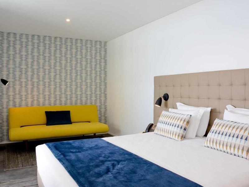 Moderne hotel lounge met twee fauteuils, salontafel, abstract schilderij en groot raam met gordijnen.