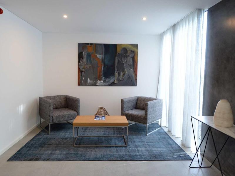 Moderne hotel lounge met twee fauteuils, salontafel, abstract schilderij en groot raam met gordijnen.