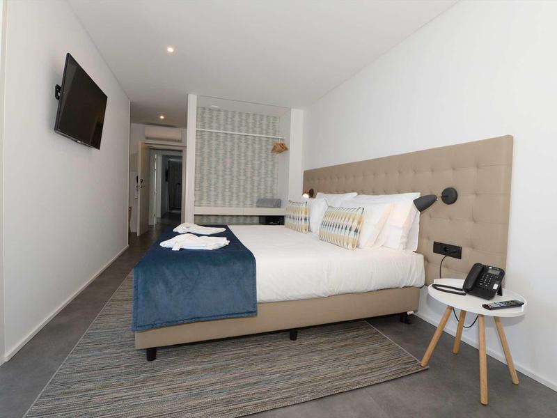 Moderne hotelkamer met tweepersoonsbed, muur-tv en nachtkastje, ingericht in neutrale tinten.