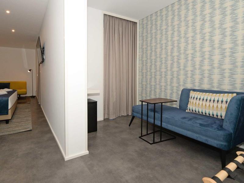 Hotelkamer met blauwe bank, patroonmuur, kleine tafel en bedgedeelte gescheiden door een halve muur.