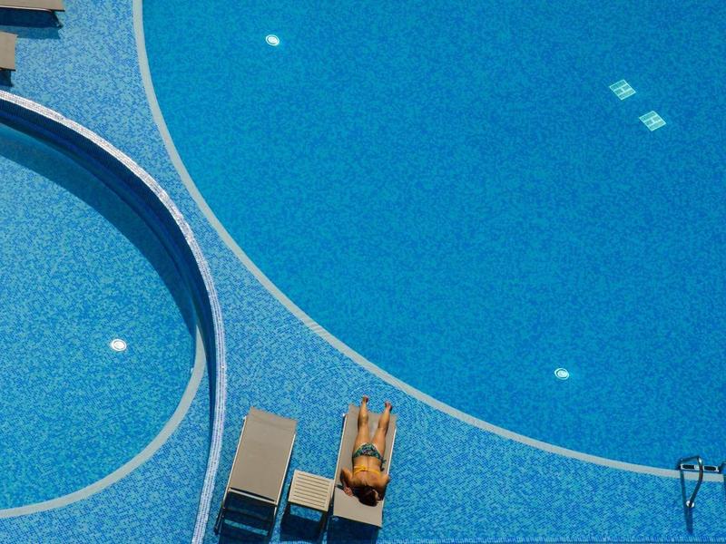 Leeg zwembad met blauw water en twee ligstoelen ernaast in zonnig weer.