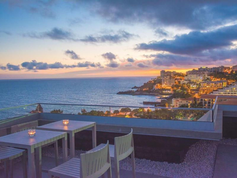 Buiten zitgedeelte met uitzicht op een kustplaats bij zonsondergang met oceaan en bewolkte lucht.