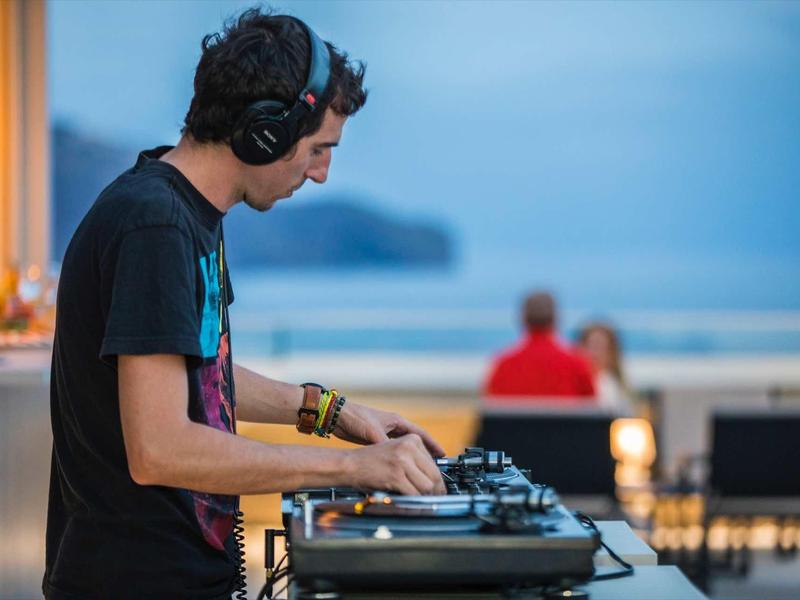 DJ draait muziek op een draaitafel bij een locatie aan zee tijdens zonsondergang.