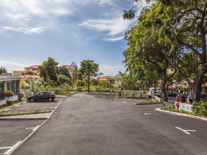 Lege parkeergelegenheid bij hotel omgeven door bomen en gebouwen onder een bewolkte hemel.