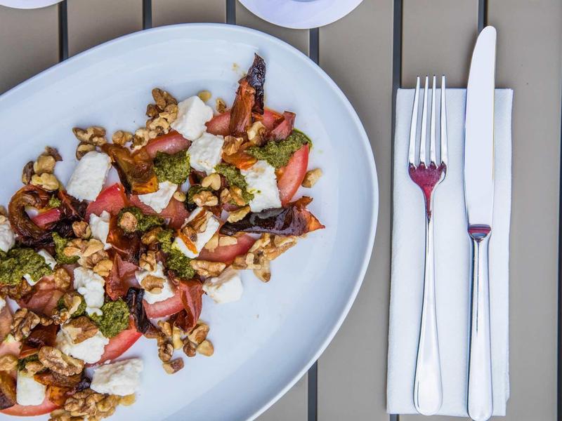 Verse salade met aardbeien, noten en kaas op een wit bord naast vork en mes op servet.