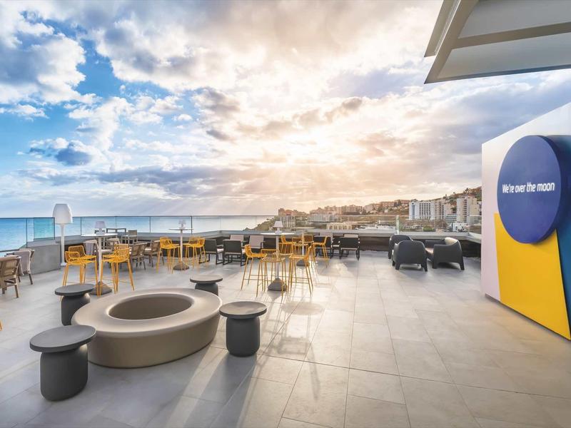 Ruim buitenterras met zitgelegenheid, vuurplaats en uitzicht op zee onder gedeeltelijk bewolkte lucht.