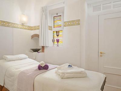 Biały pokój zabiegowy z dwoma łóżkami do masażu i złożonymi ręcznikami.