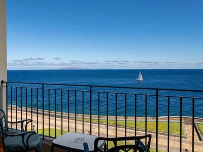 Balcony with chairs and table overlooking the sea and a sailboat on the horizon.