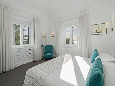 Jasna sypialnia z podwójnym łóżkiem, białymi zasłonami i turkusowymi akcentami.