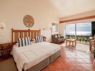 Jasny pokój hotelowy z podwójnym łóżkiem i balkonem z widokiem na morze.