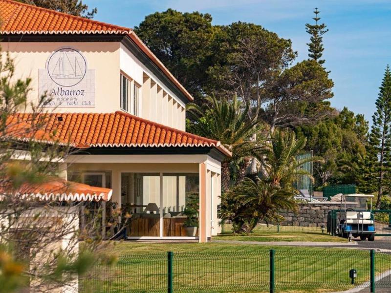 Nowoczesny budynek hotelu z czerwonym dachem, otoczony zielonym krajobrazem i drzewami.