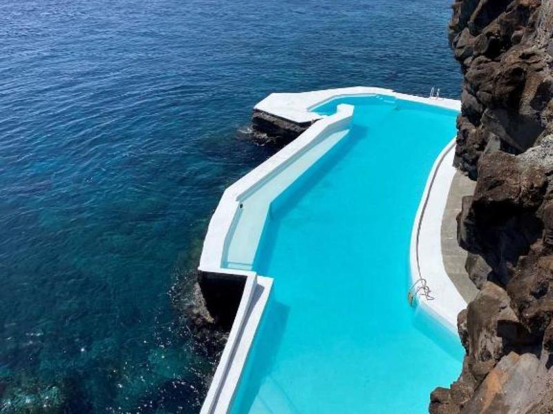 Basen typu infinity na skalistym klifie z widokiem na otwarte morze i czystą niebieską wodę.