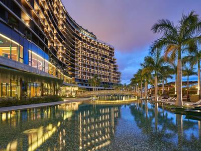 Moderní hotel s osvětleným bazénem a palmami za soumraku