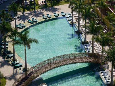 Velký bazén s mostem, obklopený lehátky a palmami v hotelovém komplexu.