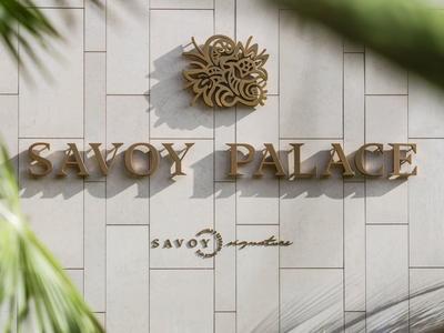 Goldfarbene Schrift und Logo an weißer Wand mit Pflanzen im Vordergrund