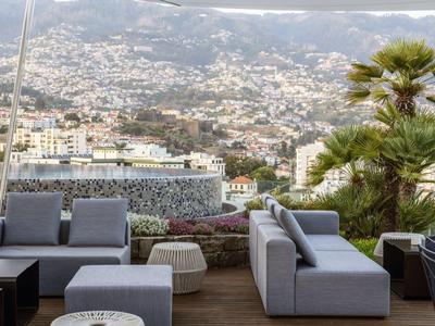 Moderní posezení na terase s výhledem na město a kopce v pozadí.