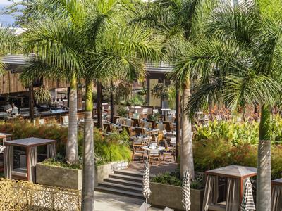 Venkovní jídelní prostor se stoly, židlemi a palmami v tropickém prostředí