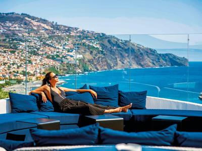 Žena relaxuje na modrém posezení s výhledem na moře a přímořské město.