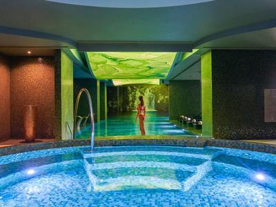 Vnitřní bazén s osvětlenými mozaikovými dlaždicemi a odpočívající osobou v pozadí