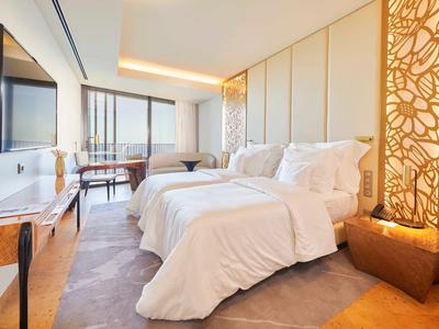 Moderní hotelový pokoj se dvěma jednolůžky, TV, psacím stolem a velkým oknem s výhledem na město.