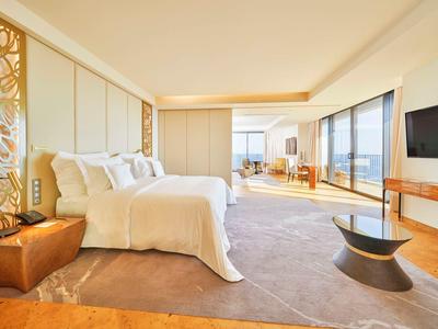 Elegantní hotelový pokoj s velkou postelí, posezením a panoramatickými okny s výhledem.