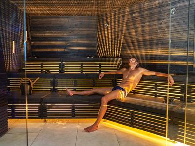 Muž odpočívá v moderní sauně s dřevěnými stěnami a nepřímým osvětlením.