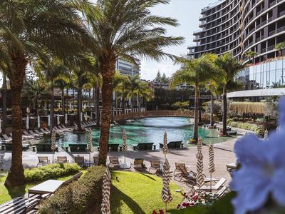 Zewnętrzny basen hotelowy z palmami i leżakami pod niebieskim niebem.