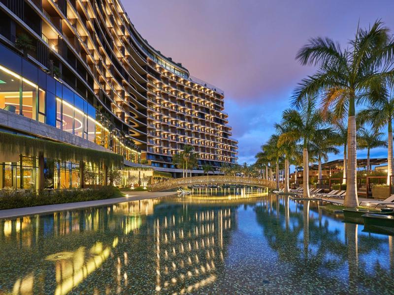 Moderní hotel s osvětleným bazénem a palmami za soumraku