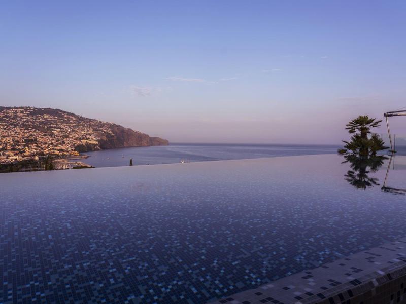 Infinity bazén s výhledem na pobřežní město a moře za jasné oblohy